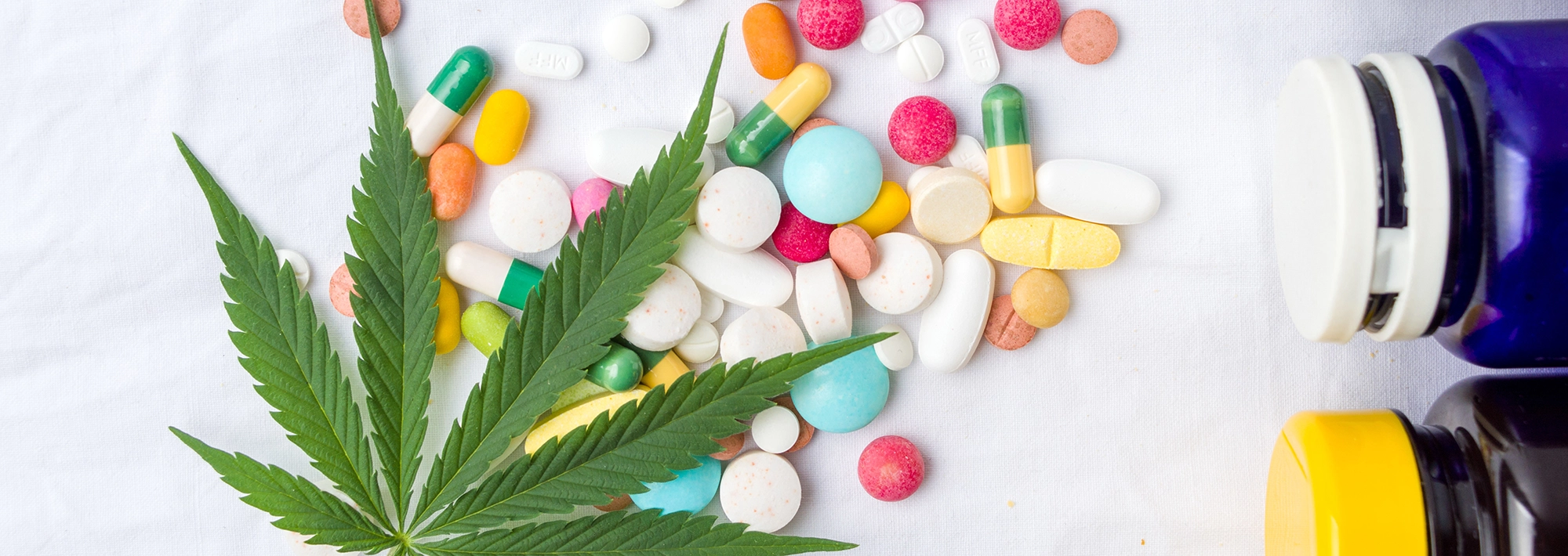 Cannabis leaf with pills and capsules in the background